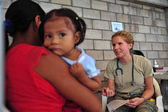 a woman holding a baby in her arms while sitting next to another woman and looking at the camera