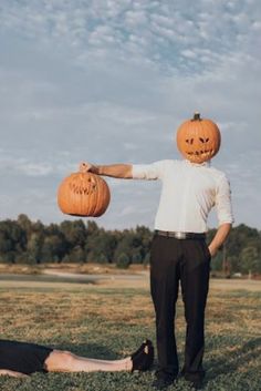 a man in a white shirt and black pants holding two pumpkins over his head