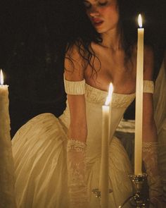 a woman in white dress sitting next to two candles