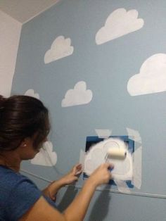 a woman is painting clouds on the wall