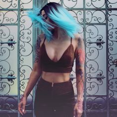 a woman with blue hair and tattoos standing in front of an iron gate wearing black pants