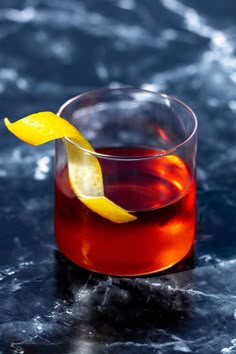 a close up of a drink with a lemon wedge on the rim and water in the background