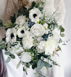 a bridal bouquet with white flowers and greenery is held by a woman in a wedding dress