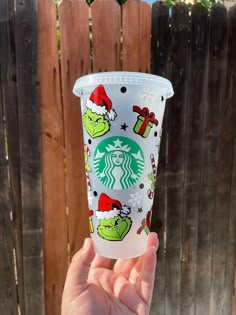 someone is holding up a starbucks cup with the grinen face on it and christmas decorations