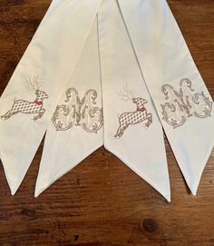 four white handkerchiefs with designs on them sitting on a wooden table next to a pair of scissors