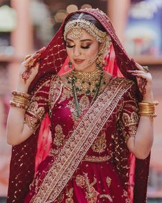 a woman in a red and gold bridal outfit is looking down at her hair