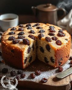 a cake with raisins cut in half on a cutting board next to a cup of coffee