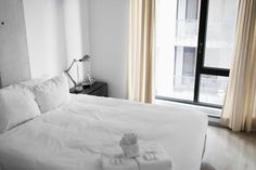 a bed with white sheets and pillows next to a window in a room that has wooden floors