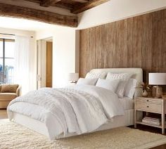 a large white bed sitting in a bedroom next to a wooden headboard and window