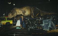 two people standing in front of a large dinosaur