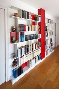 a book shelf filled with lots of books on top of a hard wood floor next to a white wall