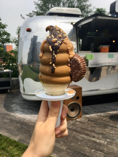 a hand holding an ice cream cone with chocolate and nuts on top, in front of a airstream