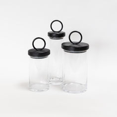 three empty glass jars with black lids on white background, one containing an o - ring