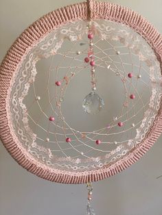 a pink and white dream catcher hanging from the ceiling with beaded details on it