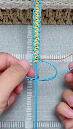 two hands are working on the end of a piece of blue yarn with yellow stitching