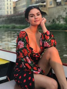 a woman sitting on top of a boat next to a body of water with buildings in the background