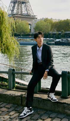 a man in a suit and sneakers sitting by the water