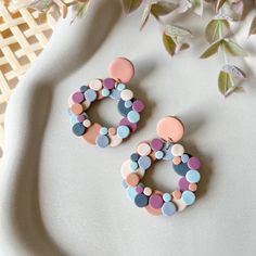 two pairs of colorful earrings sitting on top of a white table next to some flowers