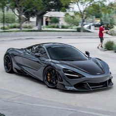 a grey sports car parked in a parking lot next to a person walking on the sidewalk