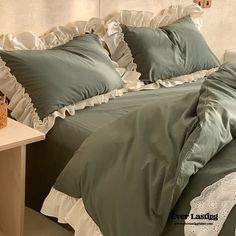 a bed with green sheets and white ruffles on the headboard is next to a night stand