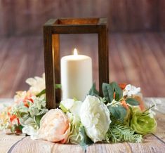 a white candle sitting on top of a wooden table next to flowers and greenery