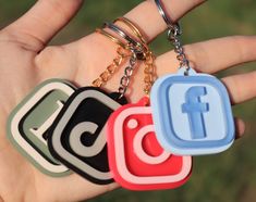 someone is holding three different key chains in their hand, one with the facebook logo on it