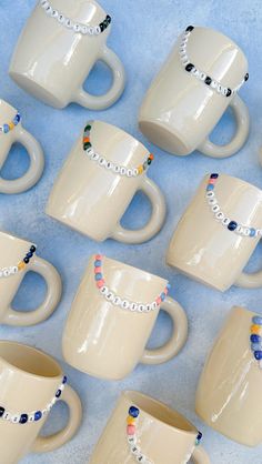 twelve coffee mugs with beaded bracelets on them are lined up against a blue background