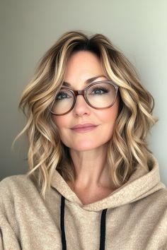 a woman with glasses and a hoodie looks at the camera while standing in front of a white wall