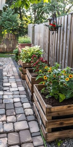 several wooden planters filled with flowers on a brick walkway next to a wood fence