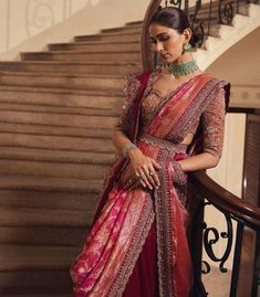 a woman in a red and pink sari standing next to stairs with her hands on her hips