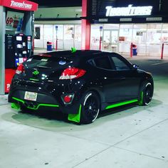 a black and green car parked in front of a gas station