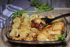 a glass casserole dish filled with pasta and meat, garnished with parsley