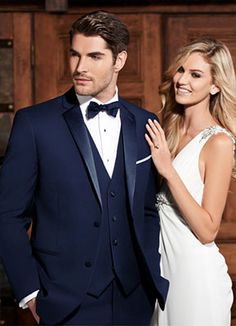 a man in a tuxedo standing next to a woman wearing a white dress