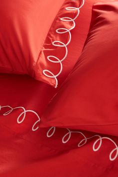 red sheets and pillows with white decorative lines on them, along with matching pillow cases