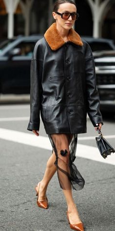 a woman walking down the street wearing a black leather coat