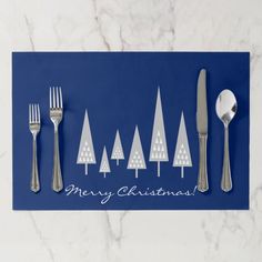 a blue christmas card with silverware and trees on the front, next to a fork and knife