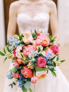 a woman in a wedding dress holding a bridal bouquet with pink, orange and blue flowers