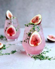 two glasses filled with watermelon and herbs on top of a white table next to sliced figs