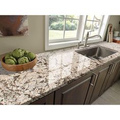 a bowl of green apples sitting on top of a kitchen counter next to a sink