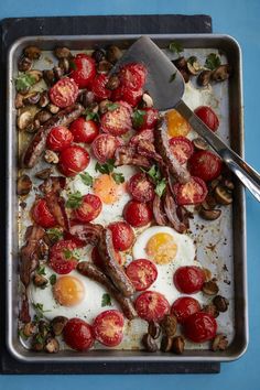 a pan filled with eggs and tomatoes on top of a blue countertop next to a spoon