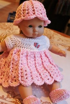 a baby doll wearing a pink dress and hat on top of a doily covered table