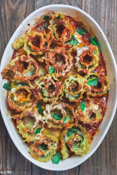 a white bowl filled with pasta covered in sauce and spinach sprinkles