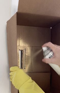 a person spray painting the inside of a cardboard box with yellow gloves and an umbrella