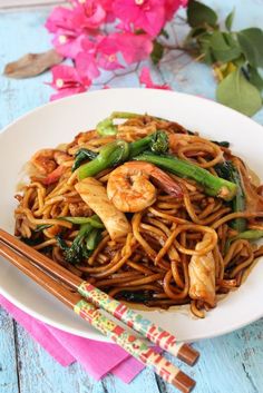 a white plate topped with noodles and shrimp next to chopsticks on a blue wooden table