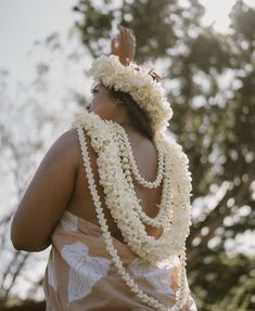 a woman in a dress with flowers around her neck and hands behind her back, looking up at the sky