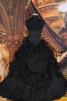 a black dress is on display in front of a wall with an ornate painting behind it