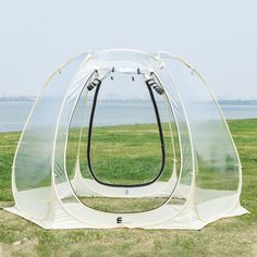 a tent that is sitting in the grass near some water on a sunny day with no one around it