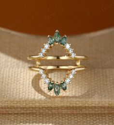 two gold rings with green and white stones on them, one is in the shape of a triangle