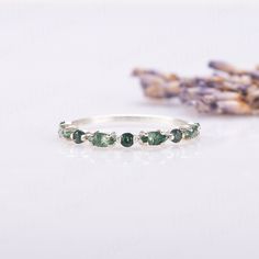 an image of a ring with green stones on the side and lavender flowers in the background