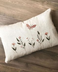 a white pillow with pink flowers and butterflies on the front, sitting on a wooden floor